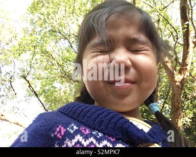 Jeune fille multi-ethnique (portrait/Punjabi/Vietnamien) visser les yeux tandis que sous un grand arbre avec des feuilles vertes au cours d'une journée ensoleillée d'automne. Banque D'Images