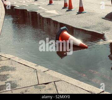 Scène de rue montrant une grande flaque après la pluie, avec un cône de circulation sur le côté dans l'eau. Bordure de la route de la chaussée et d'autres cônes sont également considérés. Banque D'Images