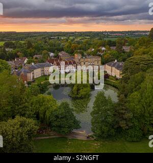 Un jeune couple assis sur un banc en face d'un lac et d'une belle rangée de maisons sous un ciel de coucher du soleil Banque D'Images