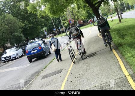 Modes de transport parallèles dans la rue : la conduite, la marche et le vélo. Les cyclistes transportant des roues de vélo sur le dos. Banque D'Images