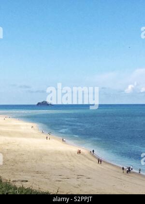 Une vue à longue distance d'une plage de sable blanc sur une île tropicale avec des gens qui marchent le long de la côte d'un océan bleu et calme à Cornwall Banque D'Images