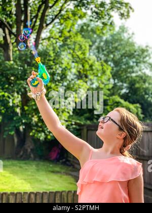 Young Girl blowing bubbles avec une arme-jouet dans jardin Banque D'Images