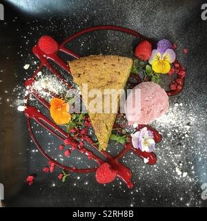 Tarte aux pistaches avec glace à la framboise, coulis de framboise et fleurs comestibles. Banque D'Images