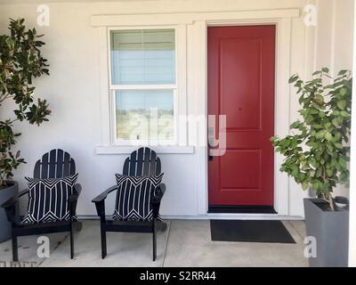 Belle véranda patio d'une maison avec des chaises de jardin, plantes en pot et une porte rouge. USA, l'Amérique Banque D'Images