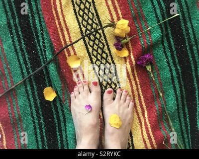 Pétales de fleurs sur les pieds d'une femme debout sur une couverture de fête. Pieds et des fleurs Banque D'Images