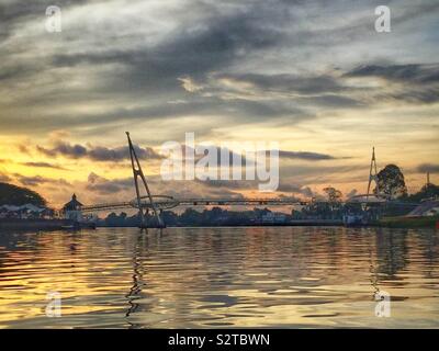 Le Darul Hana Bridge, qui permet aux piétons de traverser la rivière Sarawak, au coucher du soleil, Kuching, Sarawak, Malaisie Waterfont Banque D'Images