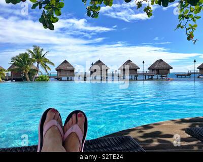 Les pieds jusqu'à la piscine à débordement tandis que d'autres kayak au bord de l'eau bungalows dans un hôtel à Moorea, Polynésie française. Banque D'Images