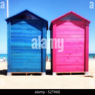 Deux cabanes en bois coloré sur une plage de sable fin, l'un bleu, l'autre rose, utilisé comme vestiaires. Banque D'Images