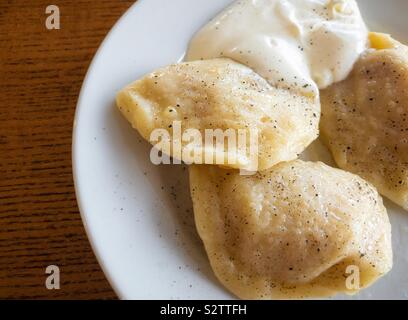 Vue de dessus sur une plaque avec vareniky ukrainien traditionnel de pommes de terre farcies de mash, manger avec de la crème, parfumée au poivre noir Banque D'Images