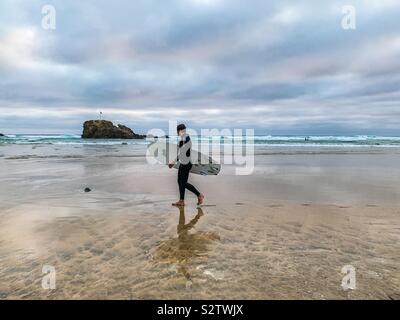 Surfer walking on beach portant sa planche de surf à Cornwall Banque D'Images
