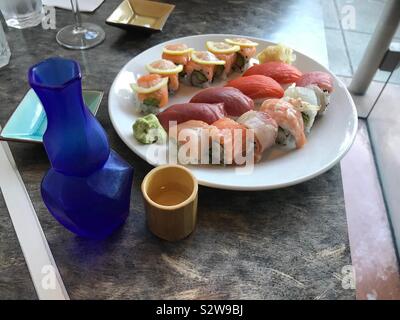 Assiette de sushis nigiri et rouleaux de sushi avec bouteille bleue de saké et small wooden cup le tableau gris. La lumière naturelle à partir de la fenêtre. Banque D'Images