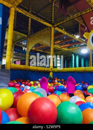 Pieds de femme avec des chaussettes rose illustré dans une piscine à balles softplay multicolores de billes en plastique à l'intérieur d'un châssis de softplay Banque D'Images