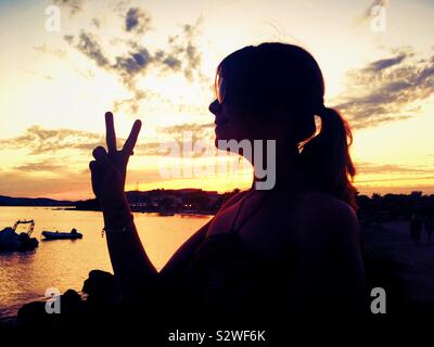 Silhouette de femme faisant signe de paix sur la plage à Ibiza au coucher du soleil. Femme hippie. L'amour et de la paix. Ibiza chill out Banque D'Images