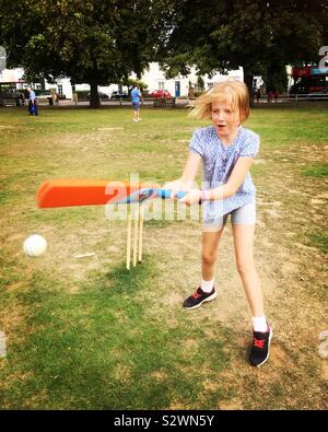 Neuf ans, fille / enfant joue cricket sur le village vert dans un jeu de cricket pour enfants avec d'autres enfants Banque D'Images