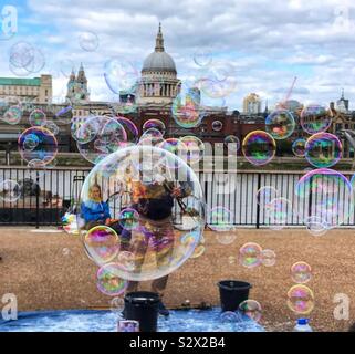 Vendeur de rue/ musicien ambulant faisant des bulles le long de la Tamise avec St.Pauls cathédrale en arrière-plan - London UK Banque D'Images