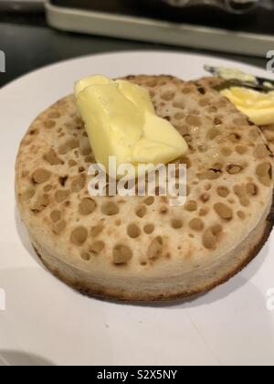 Les crumpets grillés sur une plaque blanche avec la fonte du beurre sur le dessus Banque D'Images