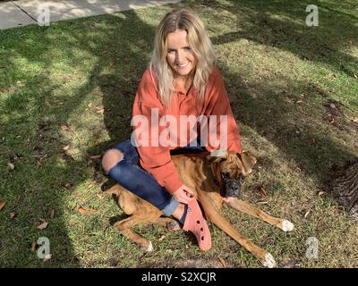 Une belle jeune fille blonde assise sur le gazon avec son chien chiot boxer bringé Banque D'Images