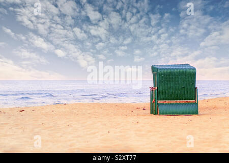 Une chaise de plage en osier vert se trouve dans le sable seul sur l'océan et jouit de la vue romantique sur la mer et le ciel nuageux Banque D'Images