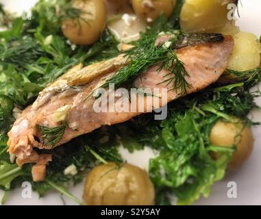 Gros plan d'une entrée gastronomique de filet de saumon poêlé sur un lit de roquette avec de nouvelles pommes de terre et d'une vinaigrette à l'ail citron Banque D'Images