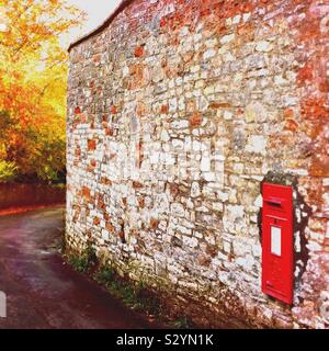 Une boîte aux lettres rouge traditionnel, encastré dans un mur sur une voie rurale Banque D'Images