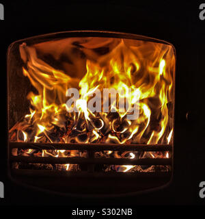Multi-carburant au bois cuisinière fire flames rage derrière le panneau de porte en verre par une froide soirée d'hiver au coin du feu à la maison à l'intérieur Banque D'Images