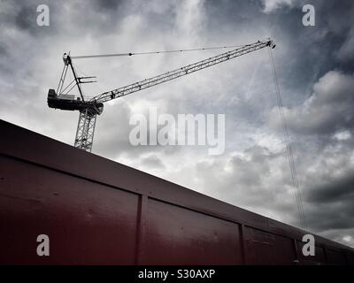 Grue de construction derrière un mur de chantier contre un ciel dramatique. Banque D'Images