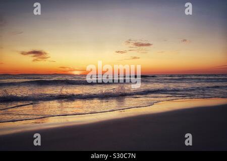 Coucher du soleil de la Californie avec des vagues se brisant sur une plage de sable. Banque D'Images