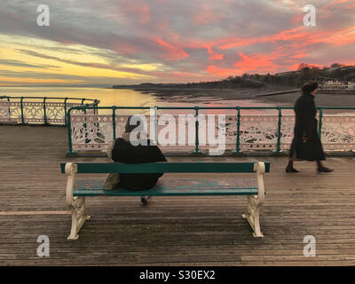 Deux dames sur Penarth pier au coucher du soleil, la marche et la lecture d'un livre, dans le sud du Pays de Galles, décembre. Banque D'Images