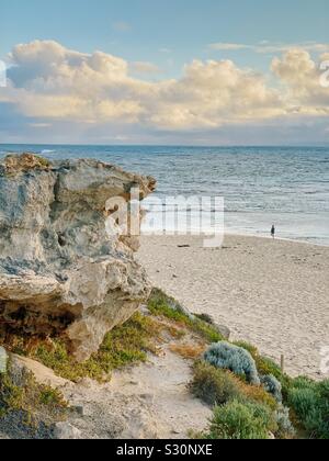 Femme seule balade au coucher du soleil sur la plage de Prevelly, Point surfeurs, l'ouest de l'Australie. Novembre 2019. Affleurement rocheux en premier plan. Banque D'Images