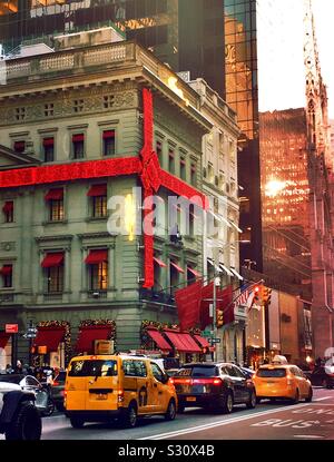 Le magasin phare de Cartier, le célèbre bijoutier est enveloppé dans un arc rouge et décoré pour les vacances pendant que le trafic se déplace sur la 5ème Avenue, New York City, États-Unis Banque D'Images