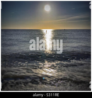 Man on a paddle board passe par la lumière solaire réfléchie sur la surface de la mer, Felixstowe. Banque D'Images