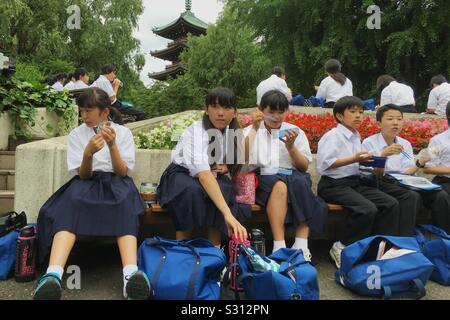 L'école japonaise les enfants mangent le déjeuner lors d'un voyage au zoo de Ueno à Tokyo, Japon. Banque D'Images