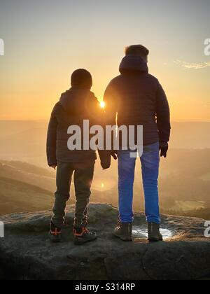 Deux garçons à regarder le coucher du soleil de Stanage Edge, Derbyshire, Angleterre, RU Banque D'Images