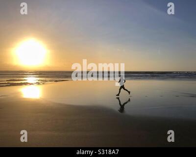 Jeune femme sur une plage de sable fin au coucher du soleil, dans le sud du Pays de Galles, janvier. Banque D'Images