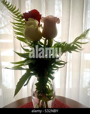 Dubuque, IOWA, 01/29/20–gros plan photo de belles roses rouges et blanches avec des fougères vertes placées dans un vase en cristal avec rose rose rose posée sur un placéme rouge brillant en premier plan. Banque D'Images