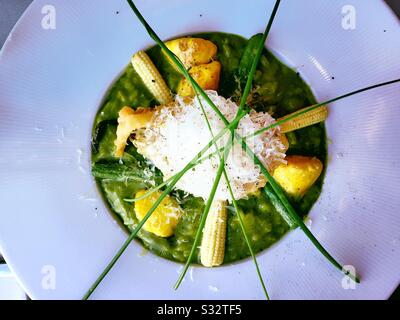 Plat se dresse près d'une entrée gastronomique de risotto aux asperges vertes servie avec du maïs bébé, des patty pan squash et des fleurs de squash, États-Unis Banque D'Images