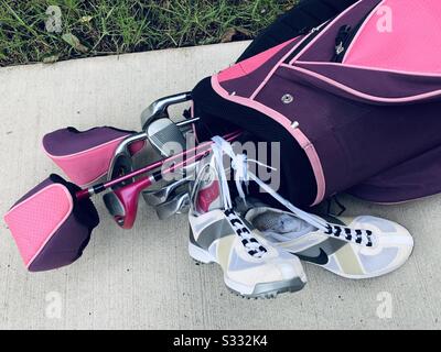 Dubuque, IOWA, 10/19--gros plan photo de l'ensemble des clubs de golf pour femmes roses et violettes avec une paire de chaussures de golf blanches et grises posée sur une allée de ciment devant l'herbe verte vive. Banque D'Images