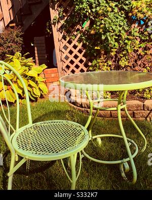 Dubuque, IOWA, 10/19--Closeup photo de verre vert et table en fer forgé et chaise à motifs devant les plantes d'automne et le treillis brun sur un jour d'automne brillant. Banque D'Images