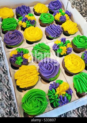 Deux douzaines de Mardi gras colorés, violets, vert citron et jaune doré, chocolat, cupcakes dans une boulangerie. Banque D'Images