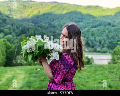 Femme en robe rose tenant un bouquet de lilas blancs Banque D'Images