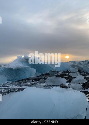 Crashing vagues sur la plage de diamant de sable noir en Islande avec coucher de soleil nuageux en hiver Banque D'Images