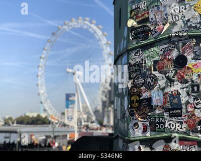 Une prise de vue sélective d'un lampadaire recouvert d'autocollants à Westminster Pier avec un London Eye flou en arrière-plan Banque D'Images