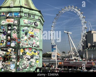 Gros plan d'un lampadaire recouvert d'autocollants touristiques avec une roue floue Millennium en arrière-plan à Westminster Pier, Londres Banque D'Images