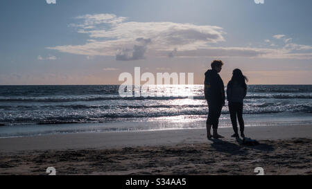 SANTA MONICA, CA, MARS 2020: Jeunes couples silhouettés lorsqu'ils parlent et regardent la mer, debout sur la plage, à côté de l'océan Pacifique, en fin d'après-midi Banque D'Images