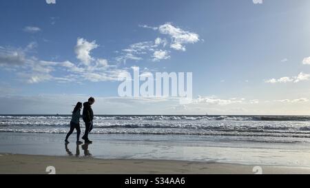 SANTA MONICA, CA, MARS 2020: Jeunes couples silhouettés lorsqu'ils marchent sur la plage, à côté de l'océan Pacifique, en fin d'après-midi Banque D'Images