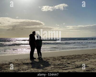 SANTA MONICA, CA, MARS 2020: Les jeunes couples silhouetted contemplent la vie tout en se tenant sur la plage, à côté de l'océan Pacifique, en fin d'après-midi Banque D'Images