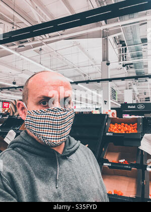 Un homme portant un masque de visage pendant qu'il fait des courses dans un supermarché en raison de la pandémie de Coronavirus l. Banque D'Images