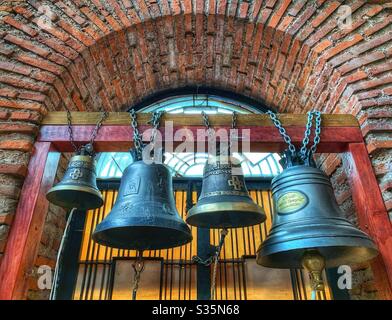 Quatre cloches enchaînées à un support en bois, entourées d'une voûte en briques. Église St George Rotonda, Bulgarie. Banque D'Images
