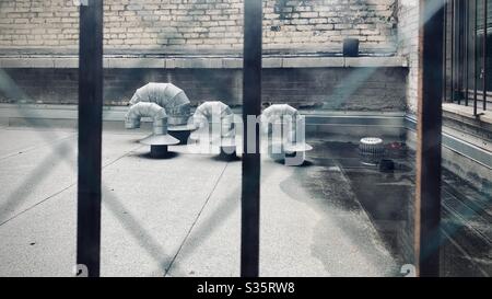 Conduits d'air métalliques recourbés sur le toit, visibles par la fenêtre avec filet de verre de sécurité et rambardes de fer à l'avant, mur de briques à l'arrière Banque D'Images