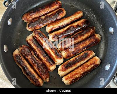 Vue rapprochée des saucisses de porc Cumberland fraîches qui se sirotent dans une poêle. Nourriture grasse et savoureuse. Petit déjeuner traditionnel anglais à base de viande dans une grande poêle à frire. Banque D'Images